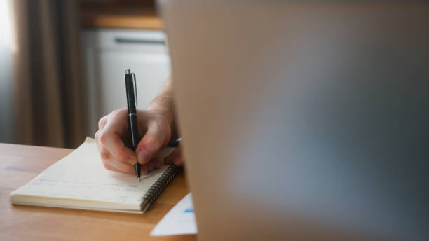 istock Close-up hand of man working at home in the kitchen with his laptop taking notes, doing research. Busy freelancer working on modern tech notebook device 1948824725