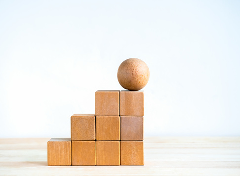 Empty blank wooden cube blocks build as a steps with the sphere one on top, isolated on wood desk on white background. Business growth process, education, success building and organizational concepts.