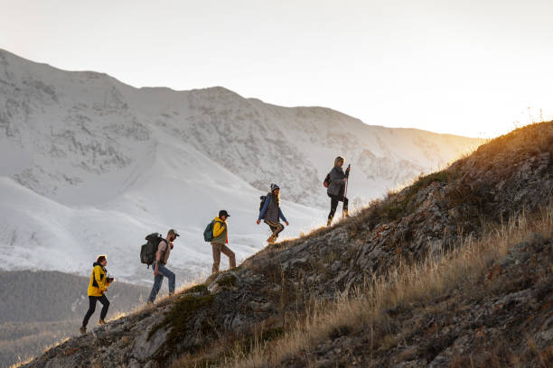 Group of active hikers walks uphill in mountains Group of young active hikers with backpacks walks uphill in mountains at sunset group mountain silhouette stock pictures, royalty-free photos & images