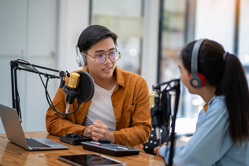 Young woman and young man wearing headphones recording a podcast in a studio
