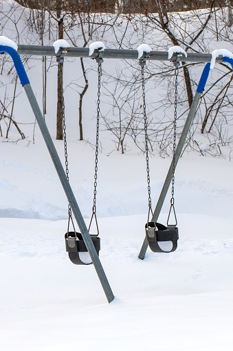 Swings at children playground in park, covered with snow in winter season. Snow day