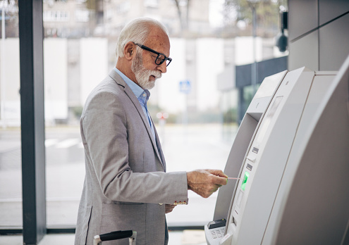 An elderly man withdraws money from an ATM with a debit card at the airport