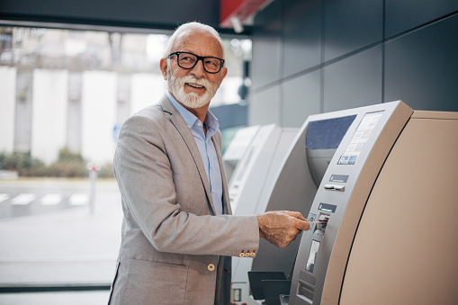 An elderly man withdraws money from an ATM at the airport