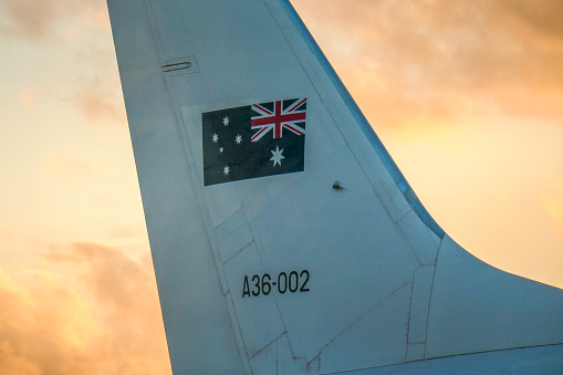 The vertical stabiliser of a Royal Australian Air Force Boeing B737-7DT (BBJ) plane, registration A36-002, used for VIP transport such as the Governor-General and Prime Minister.  She is parked at Sydney Kingsford-Smith Airport waiting to take the Governor-General to Canberra. This image was taken in the direction of the setting sun from Ross Smith Avenue, Mascot, behind a steel security fence, on a hot and sunny evening at sunset on 19 January 2024.