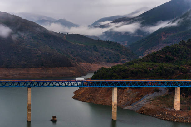 Truck with a refrigerated semi-trailer driving on a bridge over a swamp and a mountain landscape with low clouds in the background. Truck with a refrigerated semi-trailer driving on a bridge over a swamp. truck in rain stock pictures, royalty-free photos & images