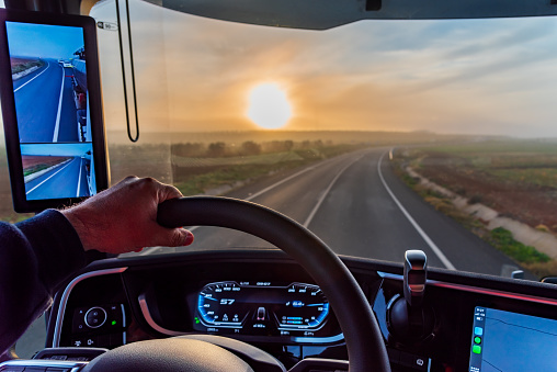 View from the driver's seat of a truck with camera rearview mirrors of a conventional road at dawn.