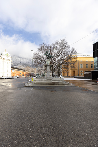 Innsbruck, Austria - February 26, 2023: Rennplatz square with Hofburg, former Habsburg palace, Leopold Fountain and Tyrolean State Theatre. Peaks of the snowy Alps mountains in the clouds in the distance