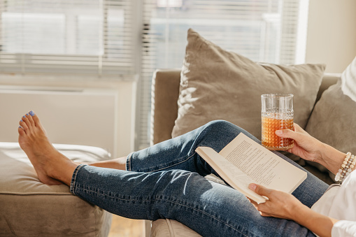 Woman enjoying a day off and reading a book on the couch in their home in New York.
