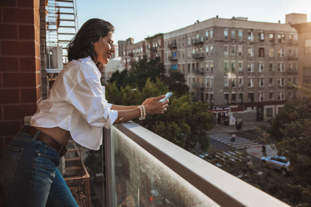 istock Woman texting on mobile while leaning on the balcony enjoying a beautiful day 1949219232
