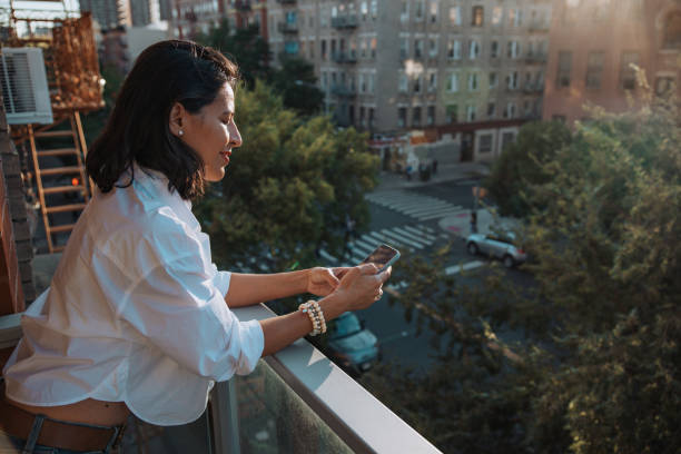 istock Woman texting on mobile while leaning on the balcony enjoying a beautiful day 1949219759