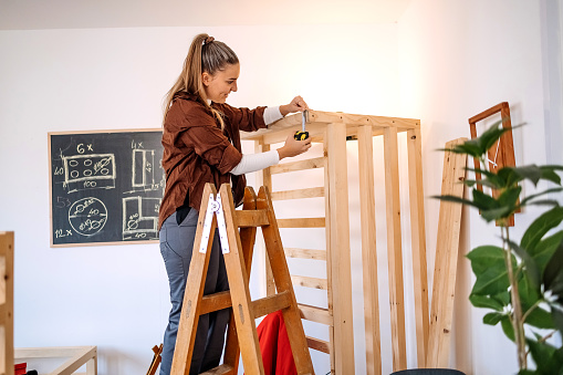 Young woman working as carpenter in her workshop checking length of wooden frame