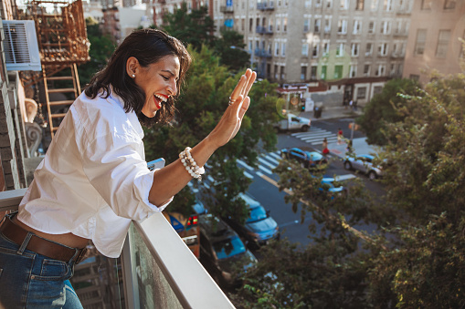Latin woman from her house in New York look out the balcony and waving to a friend downstairs.