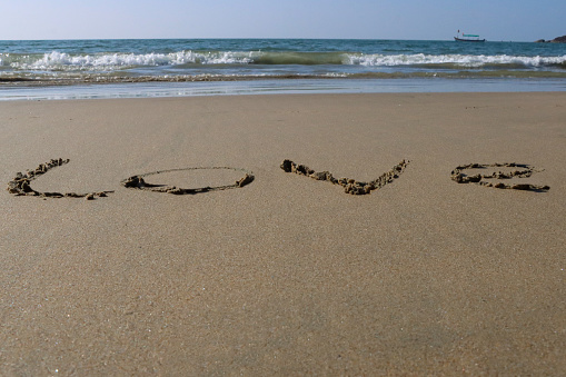 Stock photo showing writing drawn on sunny beach with word 'love' written in sand with stick in soft golden sand on seaside coastline.