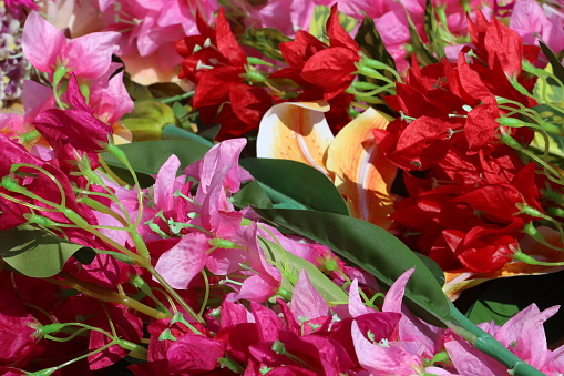 Stock photo showing close-up view of a table top covered in a pile of artificial pink, red, yellow and white long stem orchids, roses, freesias, gladioli and bougainvillea flowers. These are artificial plants made with plastic stem and leaves with silk petals.