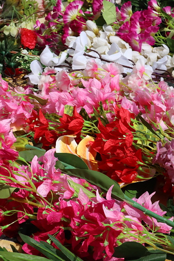 Stock photo showing close-up view of a table top covered in a pile of artificial pink, red, yellow and white long stem orchids, roses, freesias, gladioli and bougainvillea flowers. These are artificial plants made with plastic stem and leaves with silk petals.