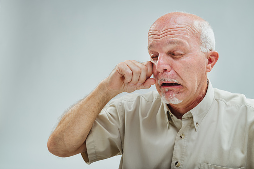 Elderly gentleman squints intensely, fingers pressing against eyes, embodying a heightened state of frustration