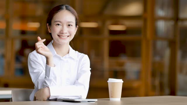 Asian woman sitting on table in front of coffee handing mini heart to camera