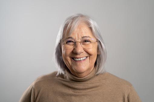 Senior woman with white hair laughing while looking at camera. Close up of smiling woman in formal wear isolated on black background.