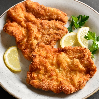 Close up view of wiener schnitzel with lemon and leaves of parsley on white plate.