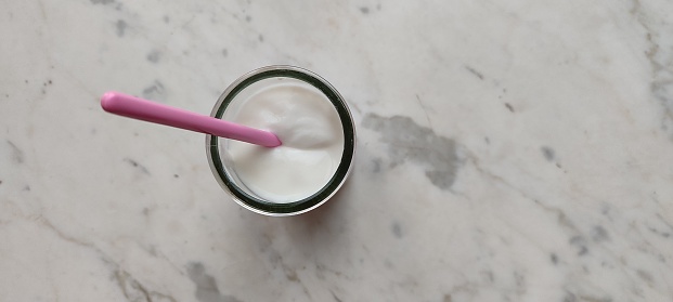 Vasetto di yogurt con cucchiaino rosa su tavolo di marmo
