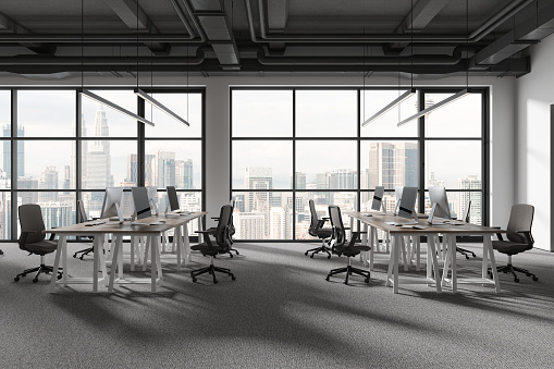 Dark coworking interior with pc computers on work table in row, carpet on the floor. Minimalist workspace with panoramic window on Kuala Lumpur skyscrapers. 3D rendering