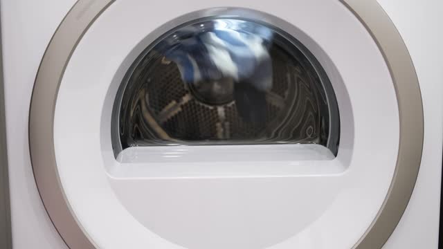 Clothes spinning in the dryer drum close-up with backlight. Housework in home laundry. Close-up view. Slow motion. High quality 4k footage