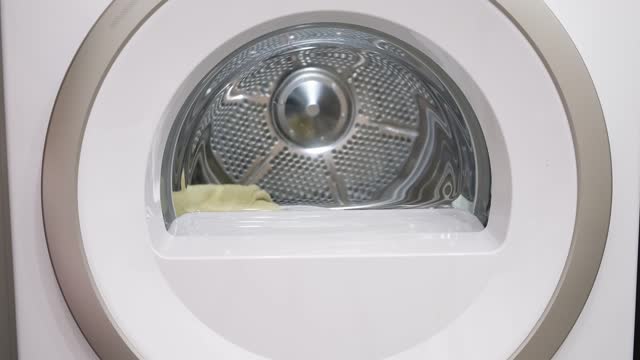 A housewife loads the dryer with clothes, turns it on and leaves, turning off the lights. Things spin in a drum. Housework in home laundry. Close-up view. Slow motion. High quality 4k footage