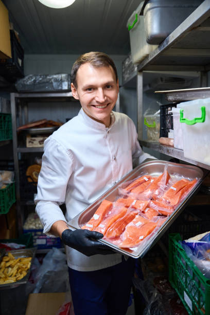 istock Man stands with tray of red fish in restaurant refrigerator 1949376766