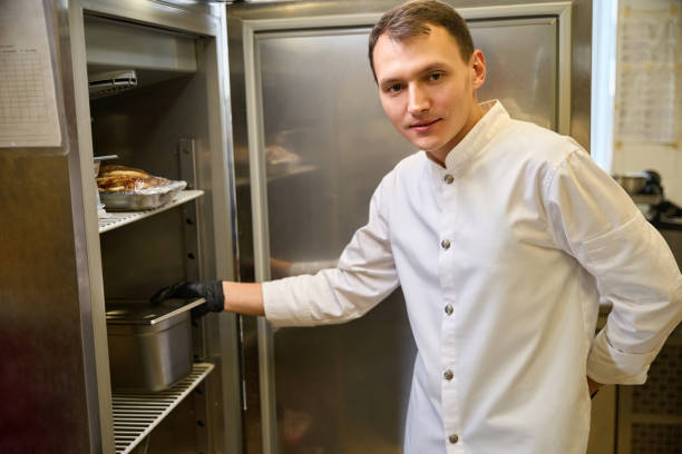 istock Cook in uniform puts a container of food in refrigerator 1949376906