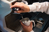 Barista in white blouse makes milk froth in coffee machine