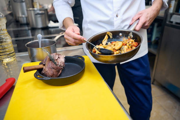 istock Kitchen employee prepares lamb shank with vegetables and sauce for serving 1949381502