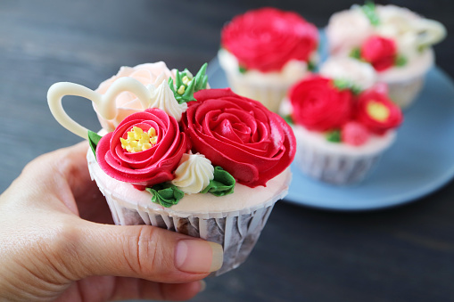 Closeup of amazing rose bouquet frosting cupcake in hand with blurry cupcakes in the backdrop