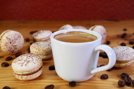 Closeup of a Cup of Frothy Hot Espresso Coffee with Heap of Tiramisu Macarons Scattered Around