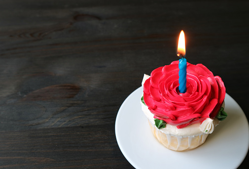 Beautiful birthday cake decorated with red rose shaped frosting with a shiny lit candle