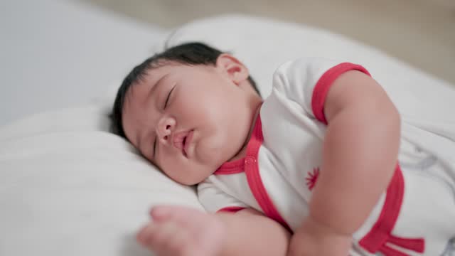 Chubby newborn baby lying on stomach, eyes open and smiling with blanket on bed.