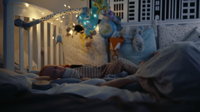 Handheld Shot of Playful Baby Boy Lying in Crib in Darkroom at Home