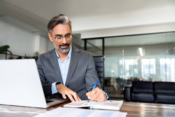 istock Middle-age Hispanic man using laptop computer for business studying, watch online virtual webinar training meeting, video call. Focused mature Indian or Latin businessman work in office, copy space. 1949502285