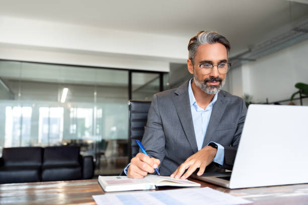 istock Middle-age Hispanic man using laptop computer for business studying, watch online virtual webinar training meeting, video call. Focused mature Indian or Latin businessman work in office, copy space. 1949502307