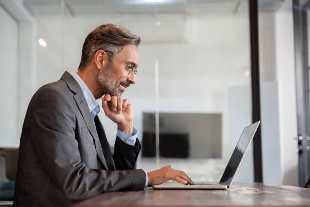 istock Mature Indian or Latin business man ceo trader using computer, typing, working in modern office, doing online data market analysis, thinking planning tech strategy looking at laptop with copy space. 1949502325