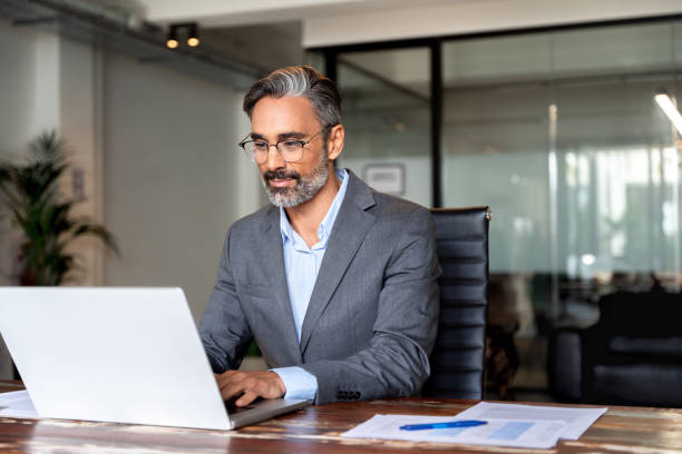 istock Happy mature European business man ceo trader using computer, typing, working in modern office, doing online data market analysis, thinking planning tech strategy looking at laptop with copy space. 1949512391
