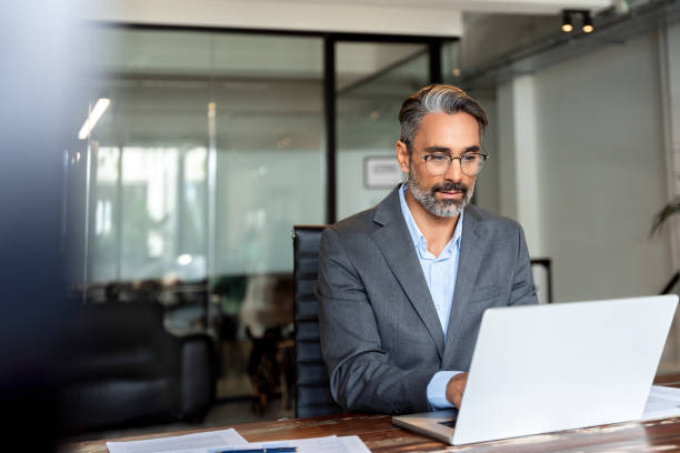 istock Happy mature European business man ceo trader using computer, typing, working in modern office, doing online data market analysis, thinking planning tech strategy looking at laptop with copy space. 1949512392