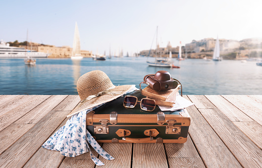 Vintage style suitcase and accessories on a wooden deck, city harbor in the background: travel destinations and vacations concept