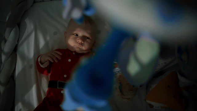 Directly Above Portrait of Playful Baby Boy in Santa Costume Lying on Crib in Darkroom at Home