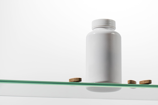 A white mock up with a jar of vitamins or medicines on a glass shelf. The concept of medicines, biologically active substances.