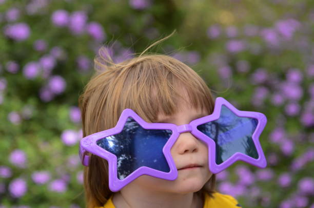 Cute kid with long hair wearing funny star glasses. The boy is preparing for the carnival in the park