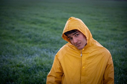 Young farmer looking at camera, yellow raincoat, sunset. document.
