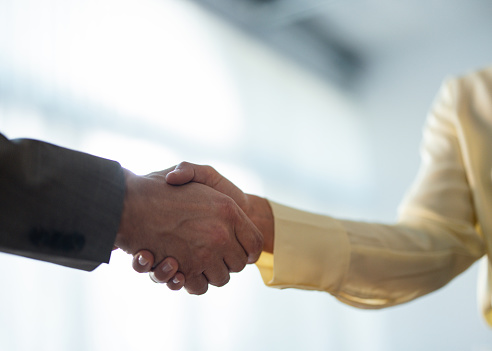 Zoomed in photo of two unrecognizable businesspeople, a man and a woman, shaking hands.