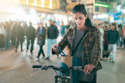 A young woman uses a bicycle while shopping in the motor vehicle-restricted area within the 15-minute  city in Himachal Pradesh for a sustainable and eco-friendly lifestyle. In the background, there is a crowd of pedestrians walking.
