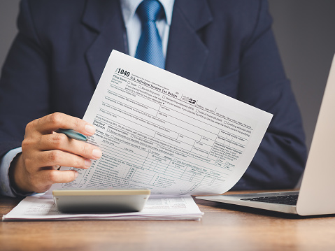 Tax day concept. A businessman in a suit holding a form 1040. U.S. individual income tax return while sitting at the table in the office. Close-up photo