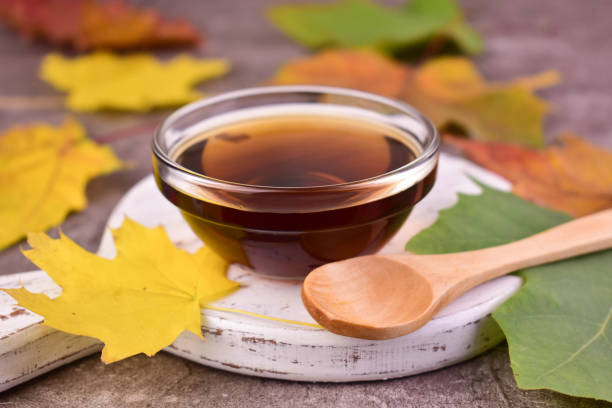 Maple syrup in a transparent bowl against a background of colorful maple leaves. stock photo